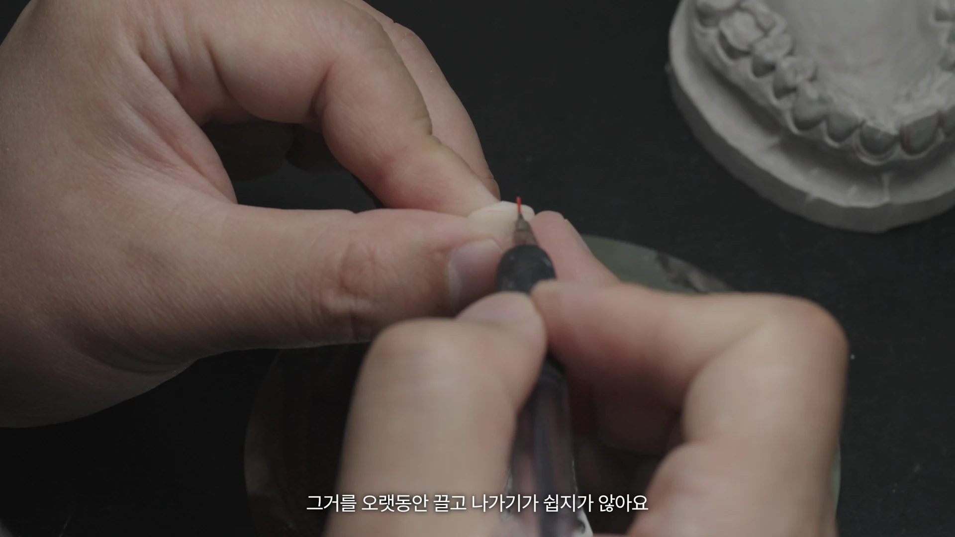작은 제작물을 손에 쥐고 도구로 세부 작업을 하는 기공실장의 손